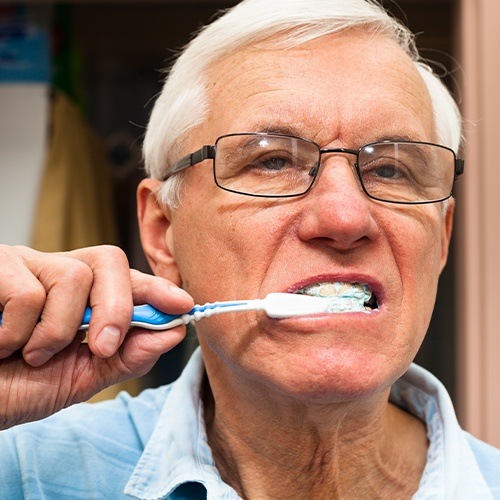 Man brushing teeth to care for his new denture