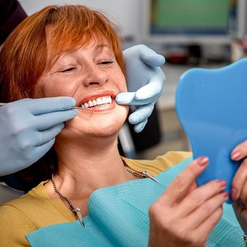 Woman looking at smile in mirror after getting dental implants in Lacey, WA