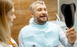 man looking in hand mirror at dentist’s office  