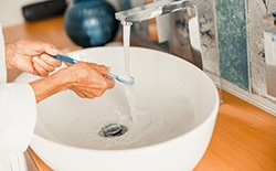 Woman practicing dental implant care in Lacey by rinsing toothbrush