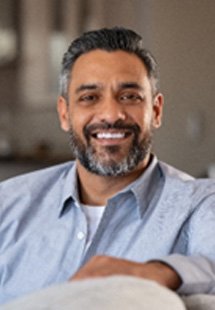 Mature man in blue shirt smiling while relaxing on couch