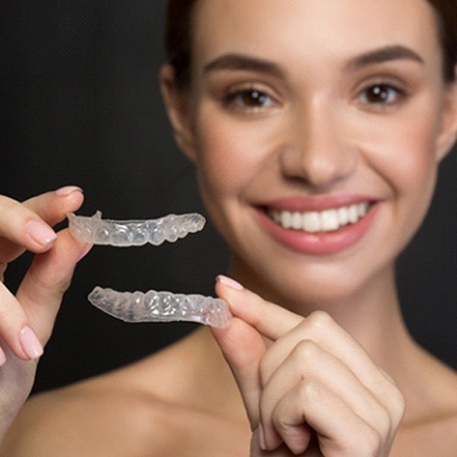 A woman holding two SureSmile aligners in Lacey