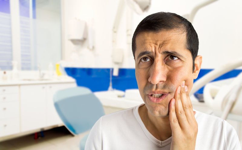 a middle-aged man holding his cheek in pain as a result of a dental injury