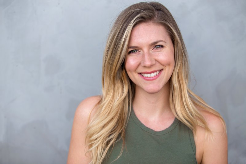 a young woman wearing a sleeveless, green blouse and showing off her beautiful smile 